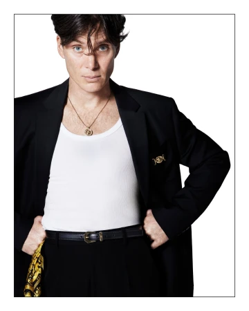 Portrait of Cillian Murphy wearing a black blazer, white tank top, and gold pendant necklace against a white background