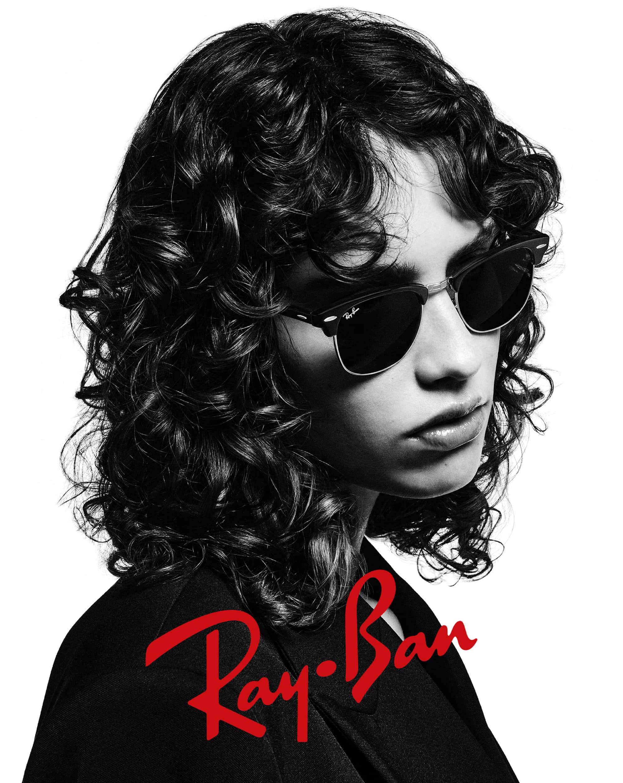 Monochrome portrait of a woman wearing Ray-Ban sunglasses, gazing slightly downward, against a bright white background with Ray-Ban logo.