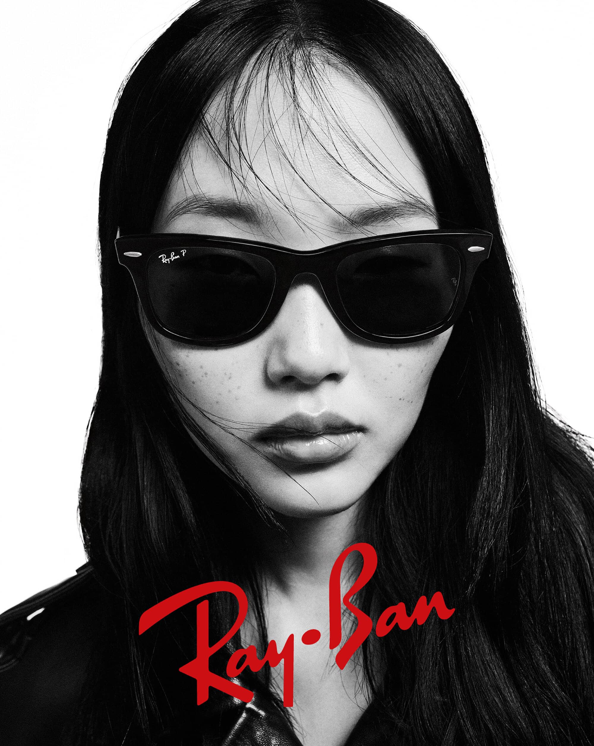 Headshot of a woman wearing Ray-Ban sunglasses with black frames, captured in a high-contrast black and white photograph. Ray-Ban logo visible.