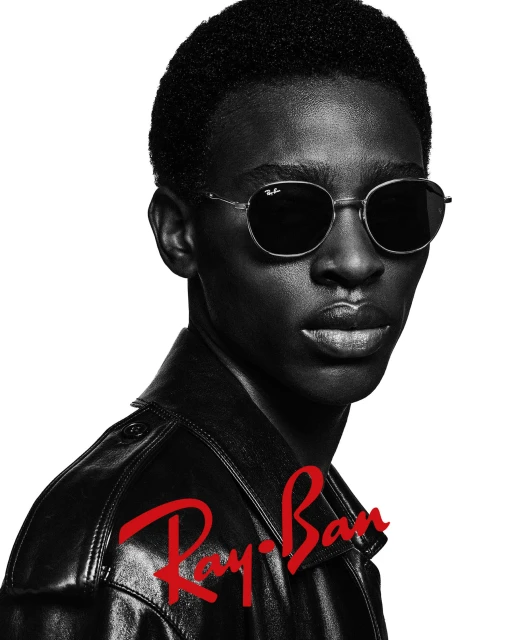 Black and white portrait of a black man wearing dark sunglasses and a black leather jacket against a plain background