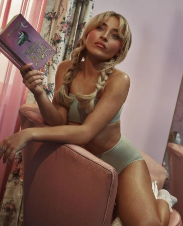 Sabrina Carpenter holding a book while kneeling on a pink velvet chair for the SKIMS Spring 2024 campaign