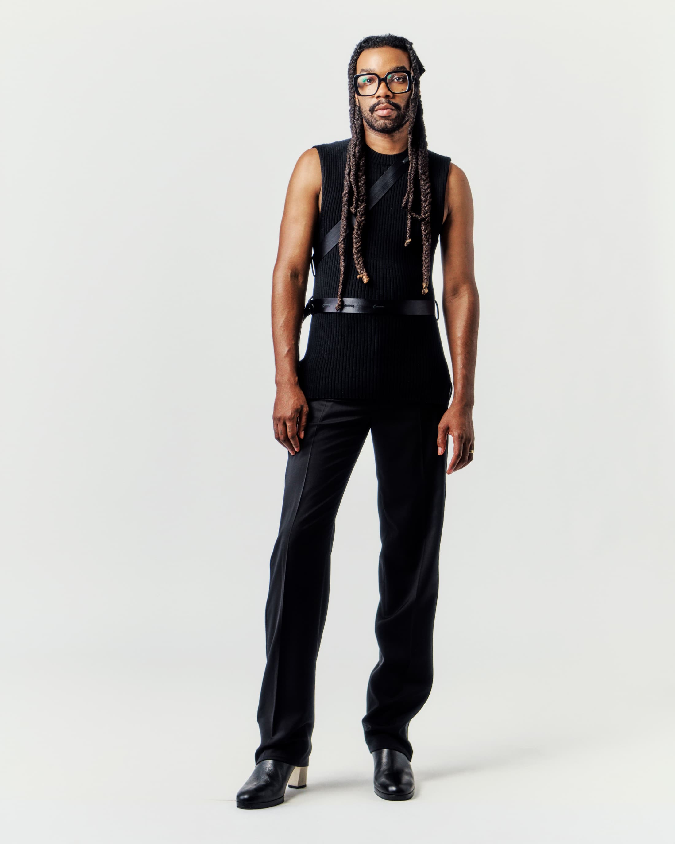 Man wearing a black sleeveless top and trousers standing against a seamless white background for Helmut Lang.