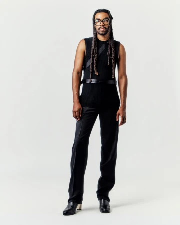 Man wearing a black sleeveless top and trousers standing against a seamless white background for Helmut Lang.