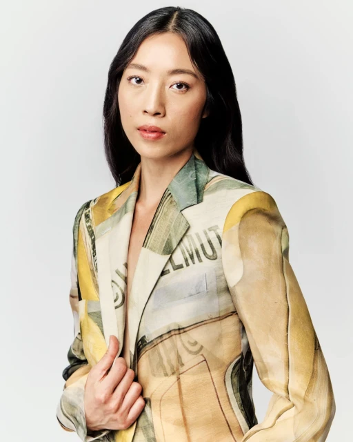 Portrait of an adult woman with black hair wearing a light-colored patterned blazer against a neutral background in a studio shot.