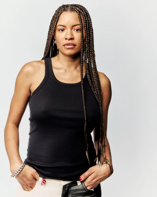 Portrait of a young adult woman with box braids, wearing a black tank top, and standing in a photo studio against a white background.