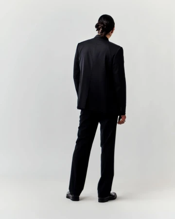 Back view of a slender adult male in a dark suit, featuring a single figure against a plain neutral backdrop in a studio setting.