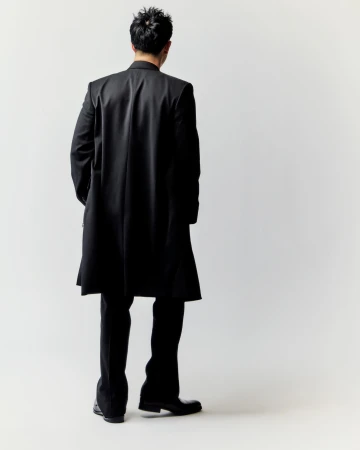 Man from behind wearing a black coat and trousers against a neutral white studio background