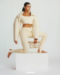 Model Imaan Hammam in cream outfit kneeling on a white block holding a patterned clutch for Jacquemus Les Sculptures campaign