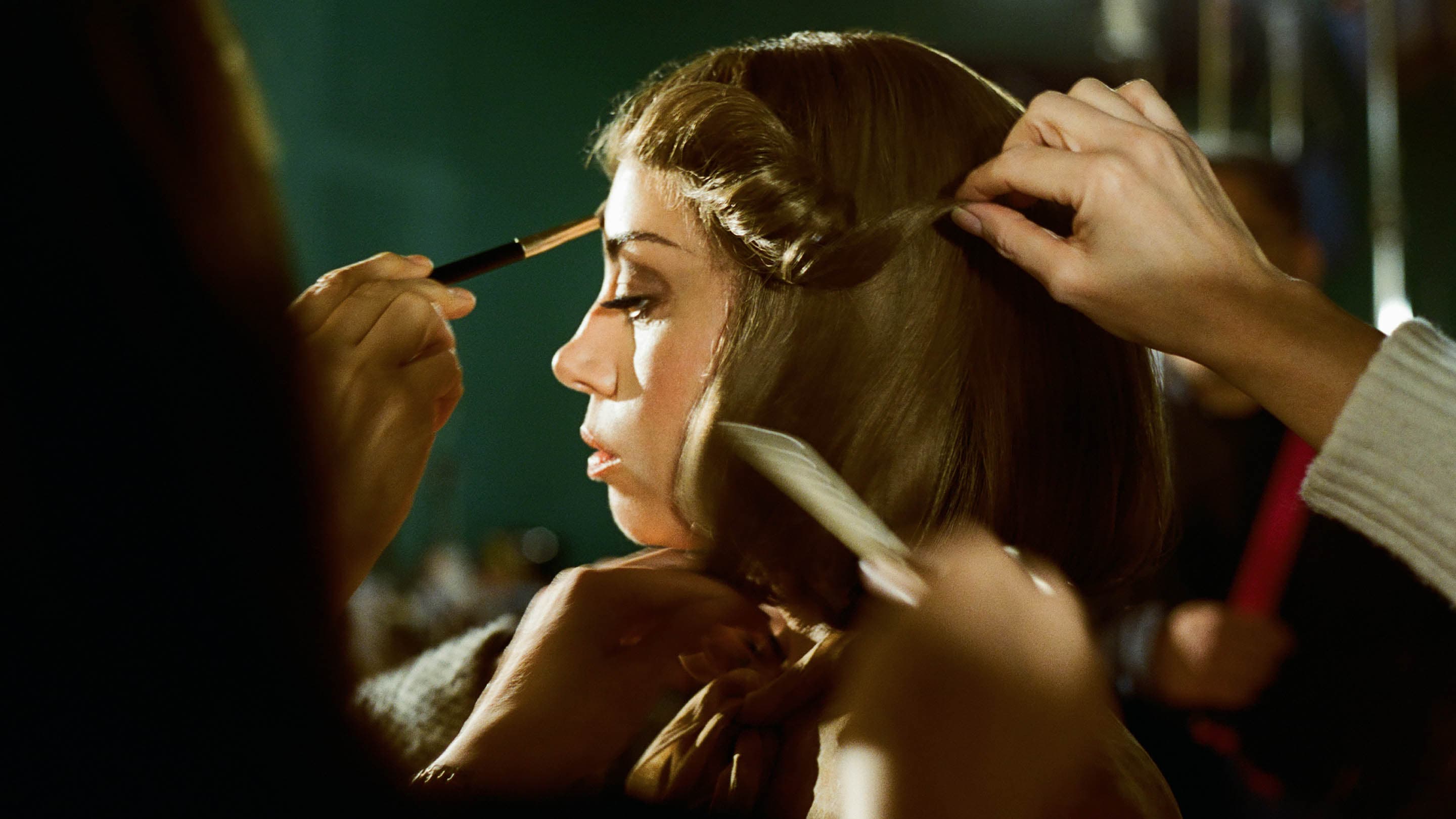Woman getting makeup applied and hair styled in a studio setting with warm lighting and a medium shot, focusing on the beauty process.