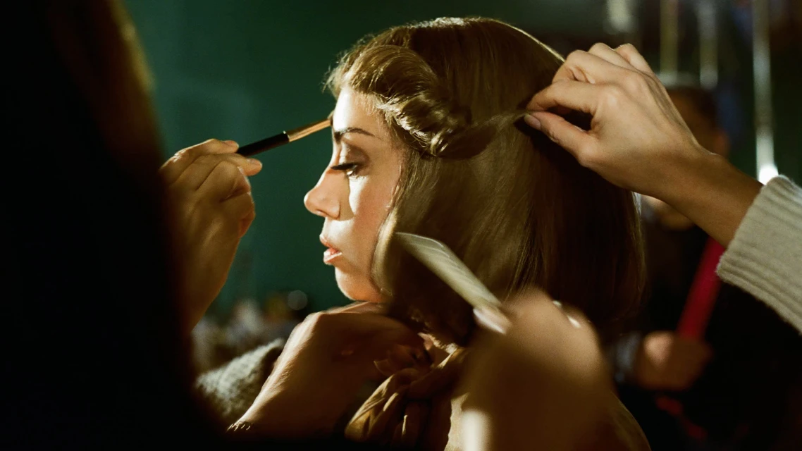 Woman getting makeup applied and hair styled in a studio setting with warm lighting and a medium shot, focusing on the beauty process.