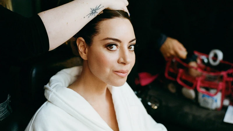 Close-up of a woman with fair skin and dark hair having her hair styled, wearing a white robe in a softly lit indoor setting.