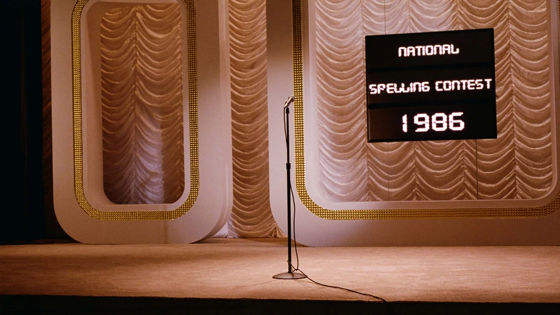 A stage with a microphone stands ready for the National Spelling Contest of 1986, lit by warm lighting. The backdrop has elegant curtains.
