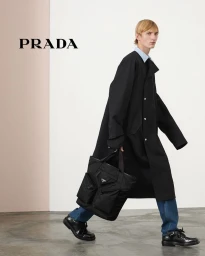 Model in black coat and blue jeans carrying a large black tote bag for Prada Spring 2024 campaign