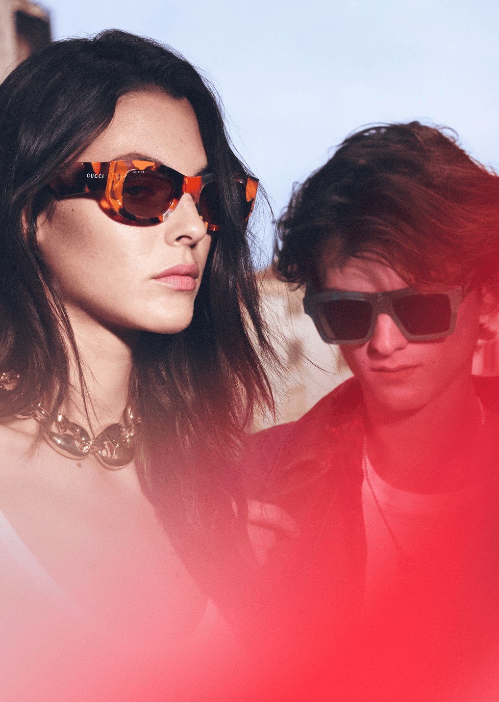 Close-up portrait of two models wearing designer sunglasses and chain jewellery outdoors under natural light.