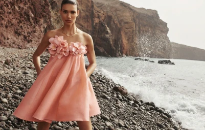Model standing on a rocky beach wearing a pink strapless dress adorned with large fabric flowers for Zimmermann spring 2024 ad campaign