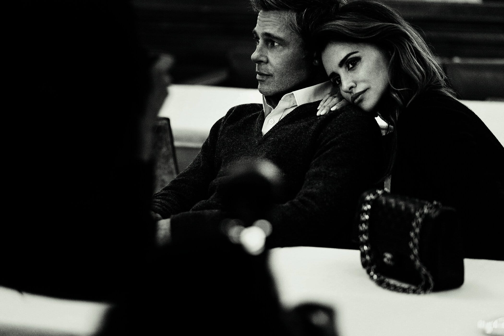 Brad Pitt and Penelope Cruz seated together in a black and white campaign portrait for Chanel featuring a quilted handbag.