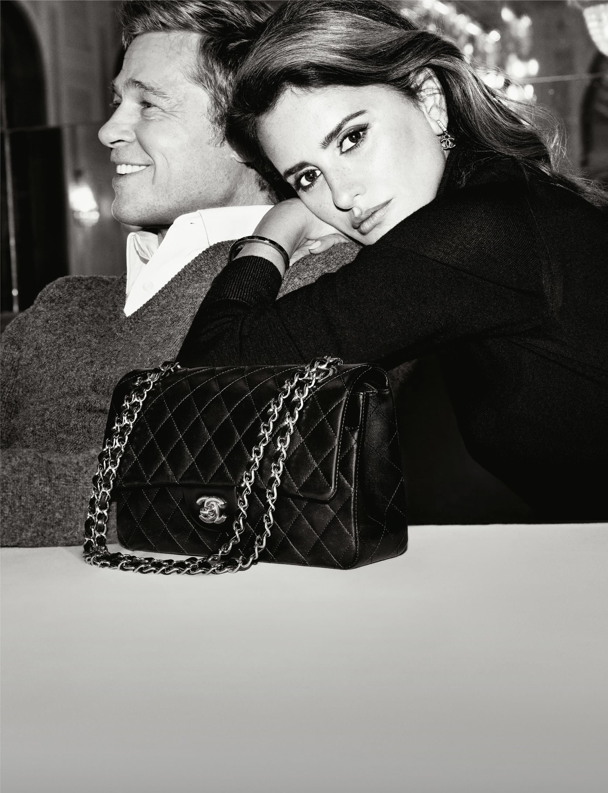 Monochrome portrait of Brad Pitt and Penelope Cruz beside a black Chanel quilted handbag, showcasing fashion and celebrity appeal.