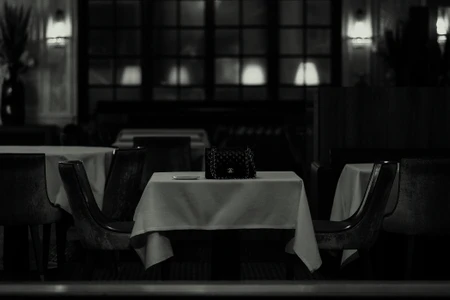 Black and white image of a Chanel handbag resting on a white tablecloth-covered table inside an interior restaurant setting.