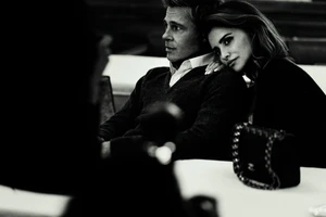 Brad Pitt and Penelope Cruz seated together in a black and white campaign portrait for Chanel featuring a quilted handbag.