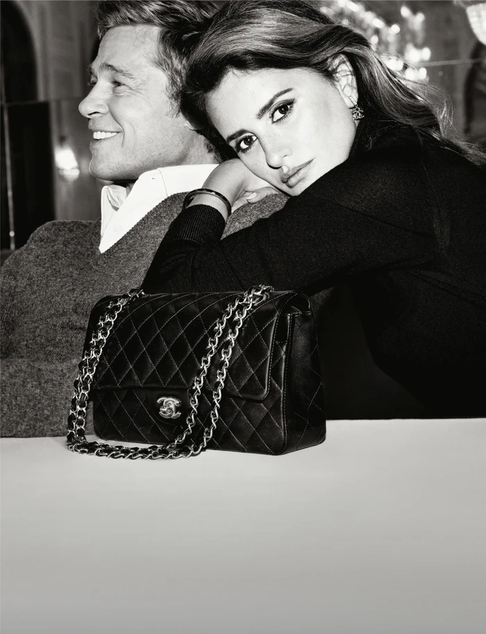 Penelope Cruz and Brad Pitt posing with a quilted leather Chanel handbag in a black and white editorial photograph.