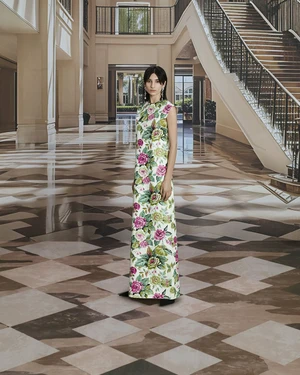 Model standing in a grand hotel lobby wearing a long sleeveless dress with an all-over floral rose print