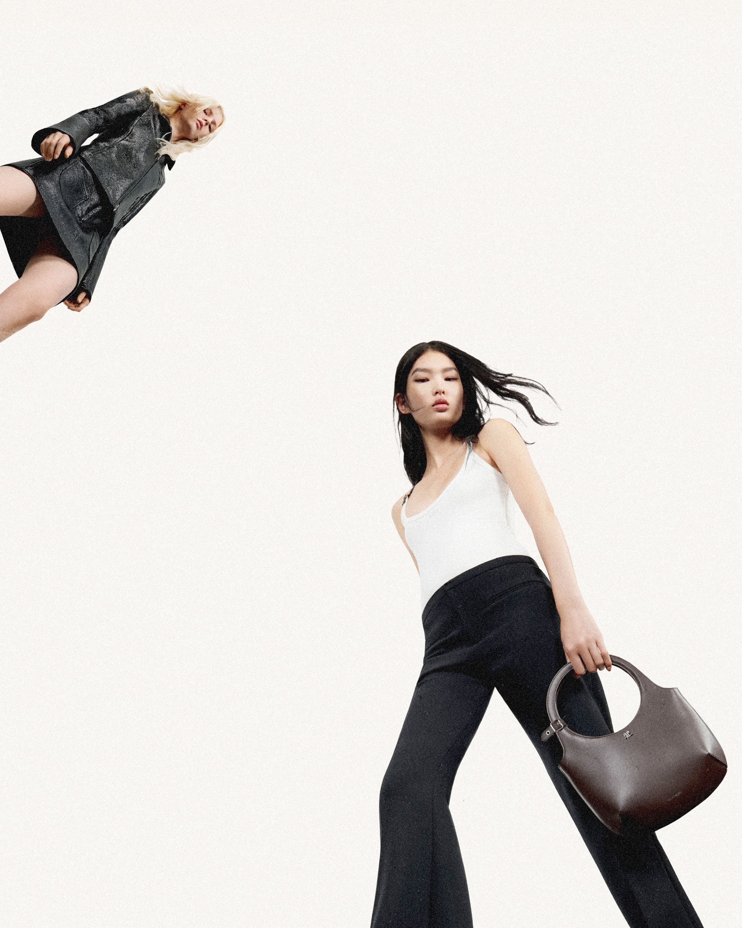 Two fashion models pose against a white backdrop, showcasing a modern handbag and stylish clothing including a black leather jacket and trousers.