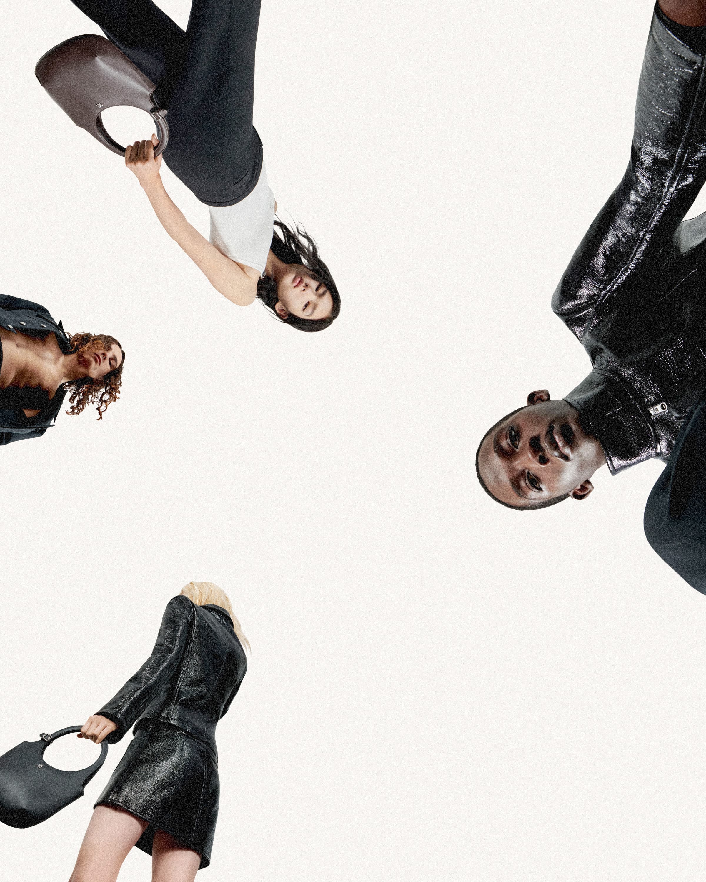 Fashion shoot featuring four diverse young adult models in black-and-white attire, accessorized with handbags, set against a bright studio backdrop.
