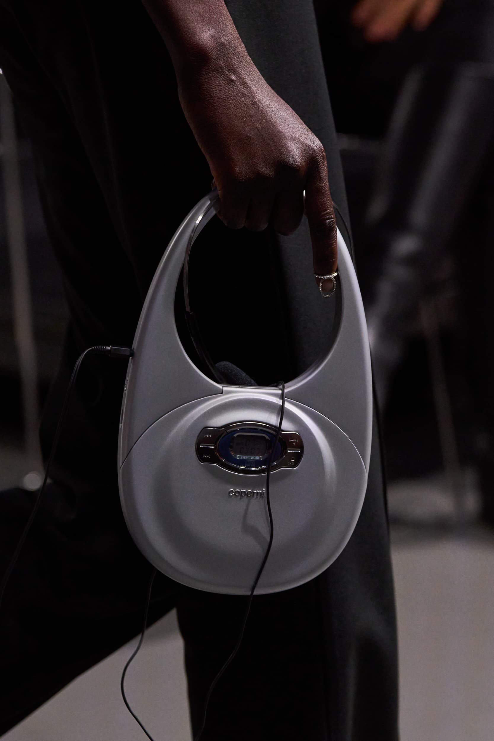 Person holds vintage personal CD player. The device is white with black cord and the person is wearing a ring.