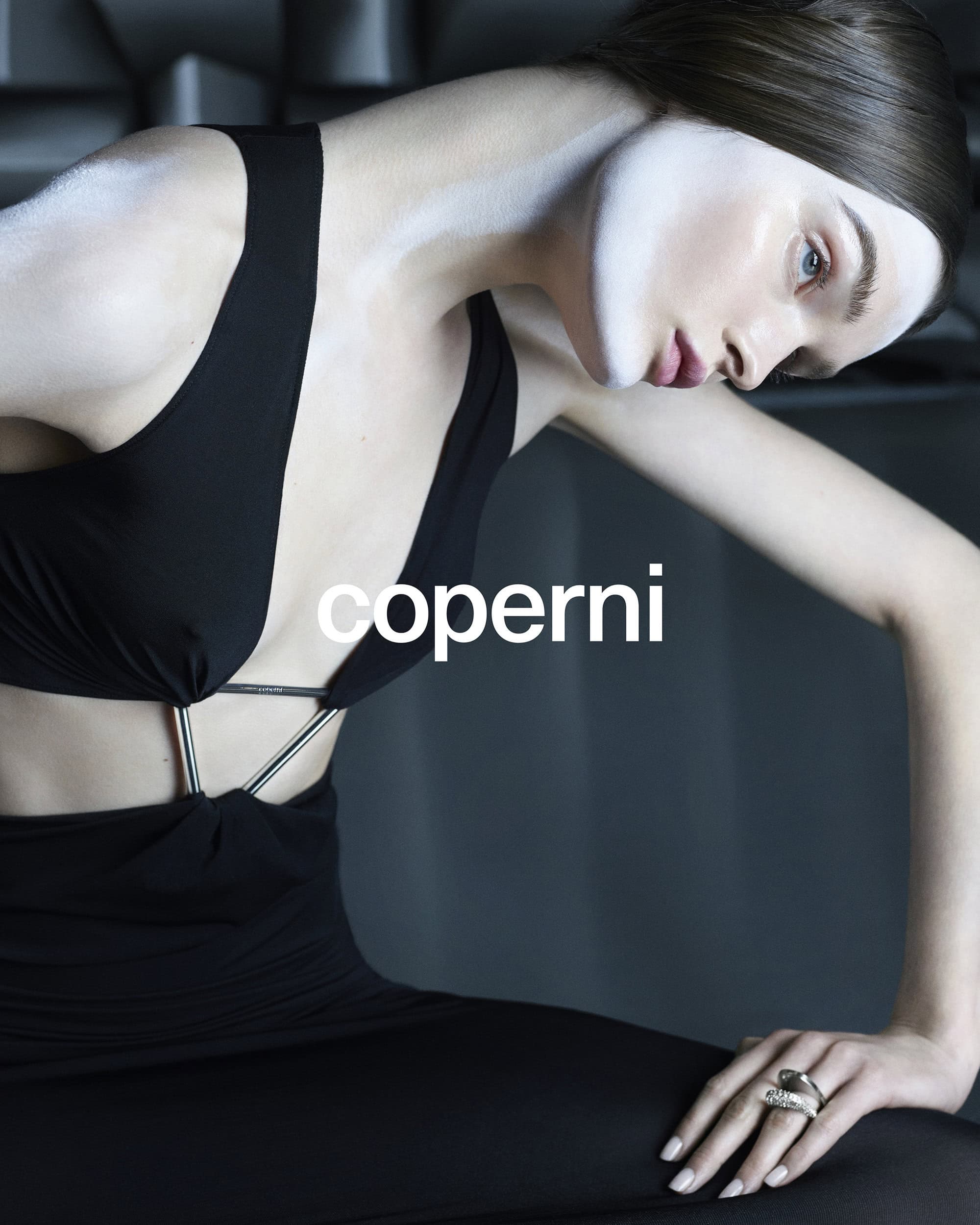 Elegant studio shot of a woman wearing a black dress and jewelry, gazing downward with soft lighting and a textured background.