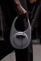 Close-up of a person holding a silver CD player shaped handbag for the Coperni Spring 2024 campaign