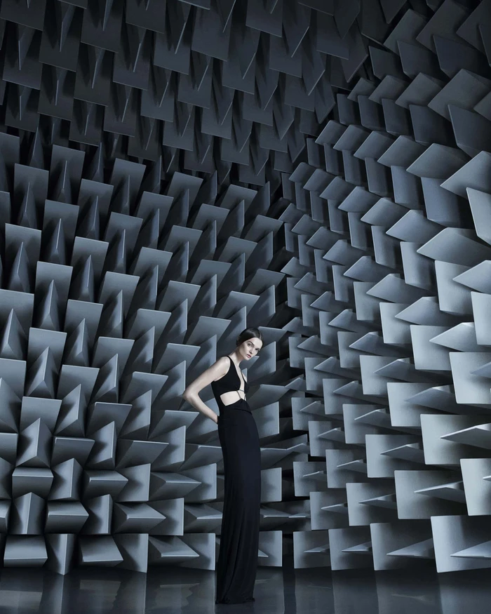 Model in a black gown standing against an intricate geometric acoustic wedge wall for Coperni Spring 2024 campaign