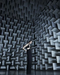 Model in a black gown standing against an intricate geometric acoustic wedge wall for Coperni Spring 2024 campaign
