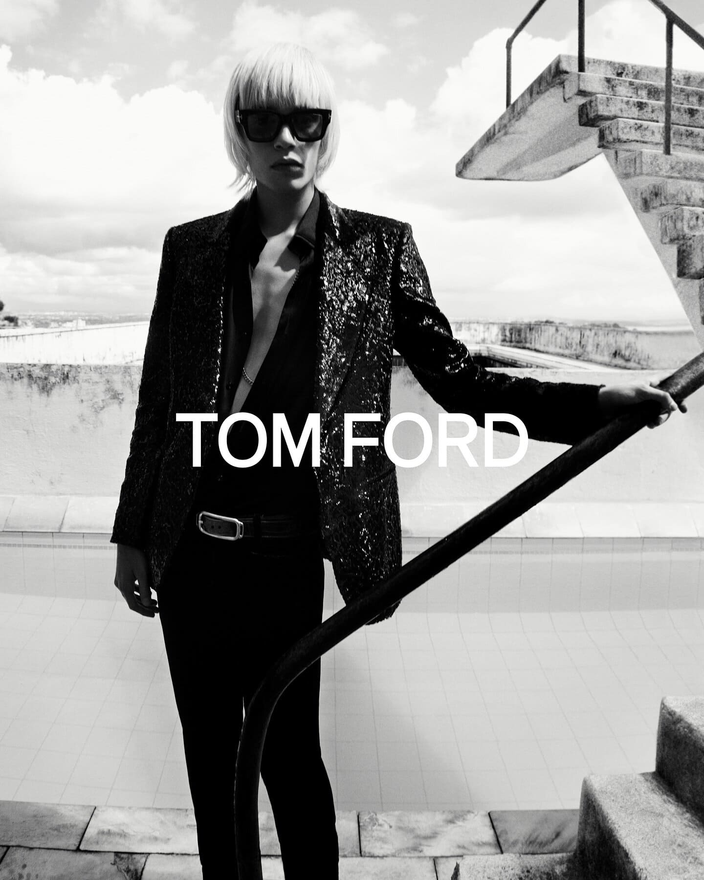 Black-and-white fashion shot of an adult female model in sunglasses, wearing a sequined blazer, standing on stairs. Tom Ford logo.