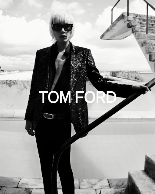 Black-and-white fashion shot of an adult female model in sunglasses, wearing a sequined blazer, standing on stairs. Tom Ford logo.