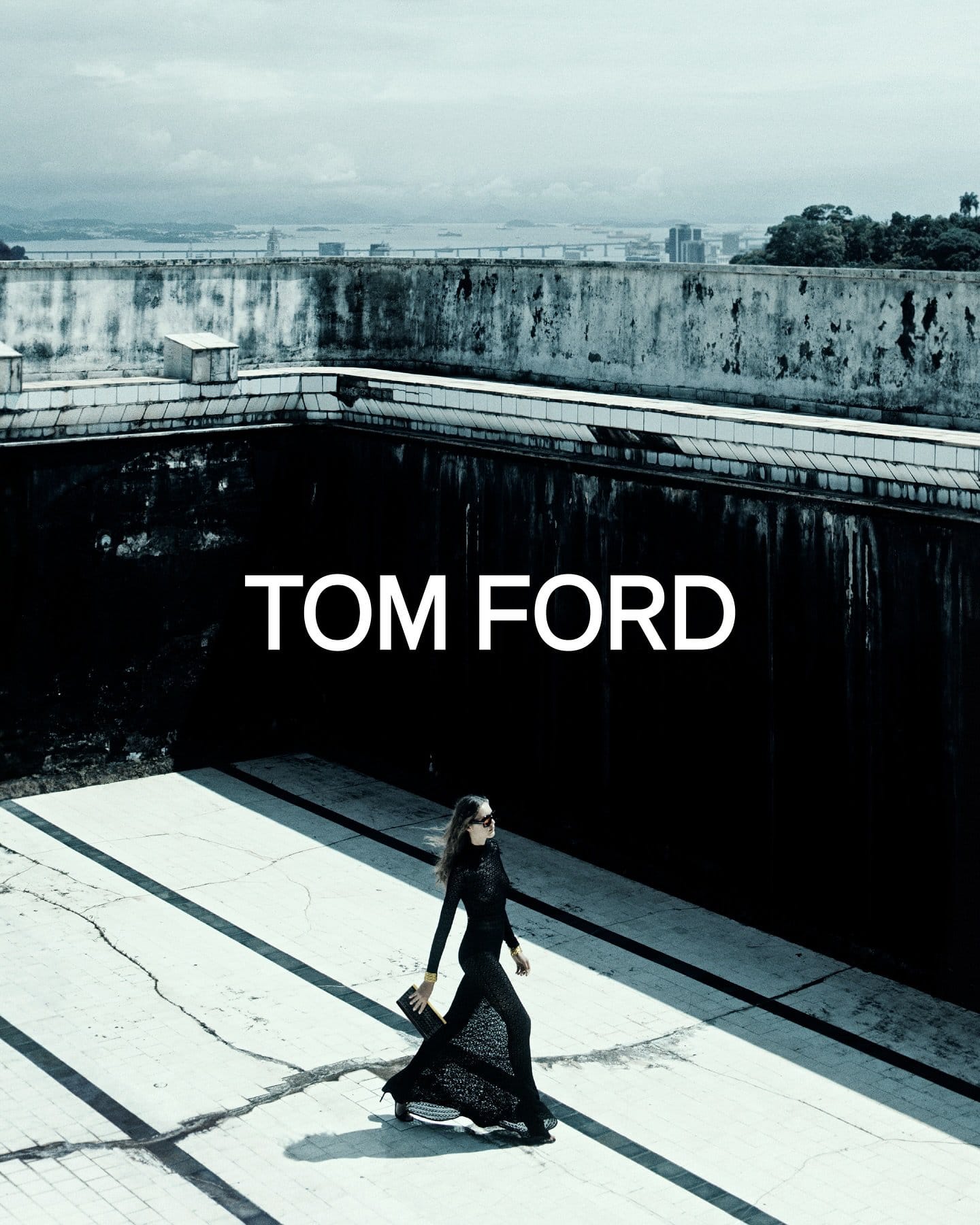 Model in black clothing walking across a concrete rooftop with urban background for Tom Ford