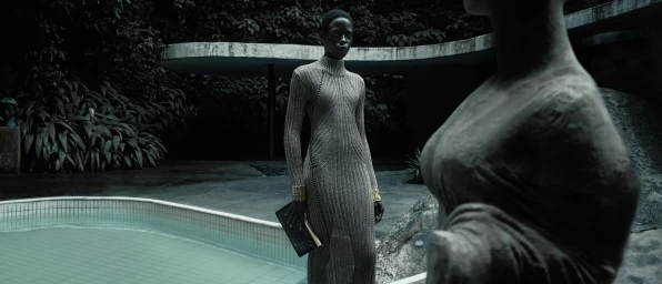 Model standing outdoors near a pool wearing a textured metallic knit dress, holding a dark clutch for Tom Ford