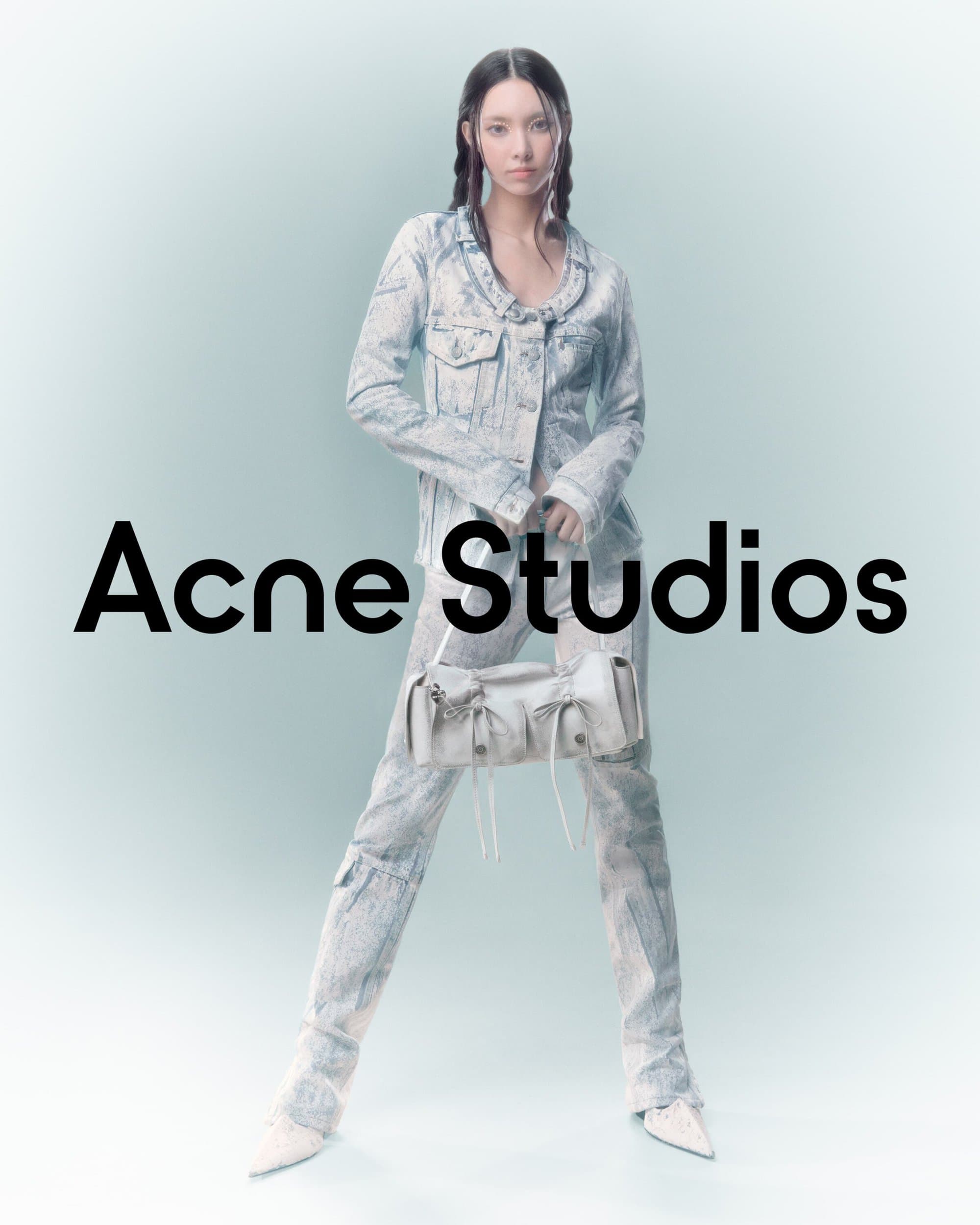 A woman poses in a light-blue tie-dye denim jacket and pants, holding a light-colored bag with black Acne Studios text overlayed.