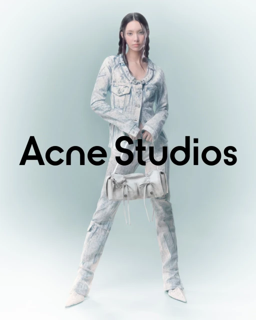 A woman poses in a light-blue tie-dye denim jacket and pants, holding a light-colored bag with black Acne Studios text overlayed.