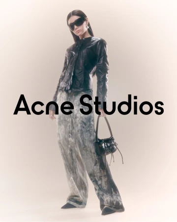 Fashion model in runway pose wearing a black leather jacket, grey printed trousers, and sunglasses holding a black purse.