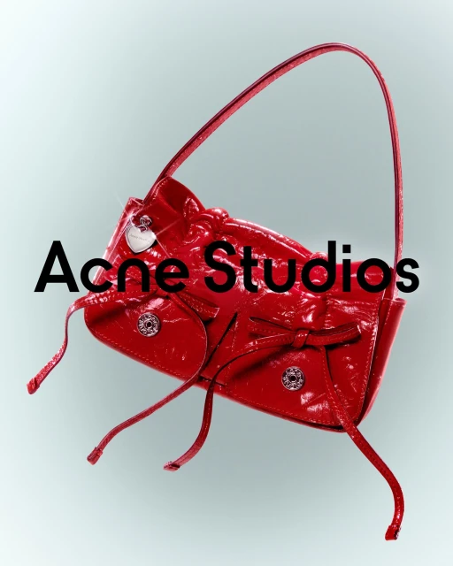 Red patent leather handbag with bows and silver hardware floats against a graduated grey background in a studio product shot.