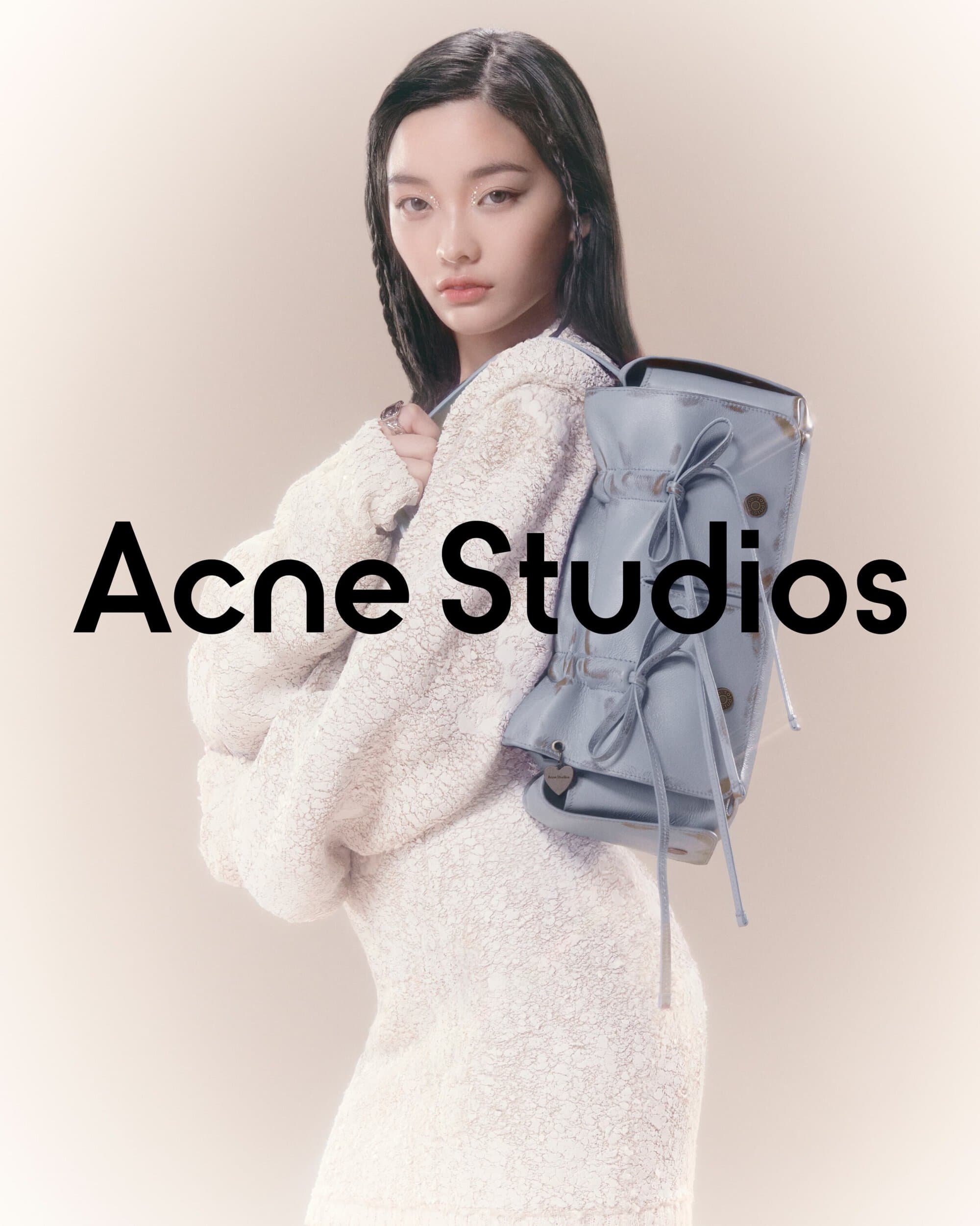 A young adult woman with black hair and a light complexion poses with a light blue backpack and a white dress in a studio setting.