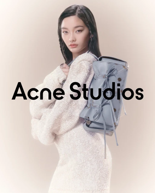 A young adult woman with black hair and a light complexion poses with a light blue backpack and a white dress in a studio setting.