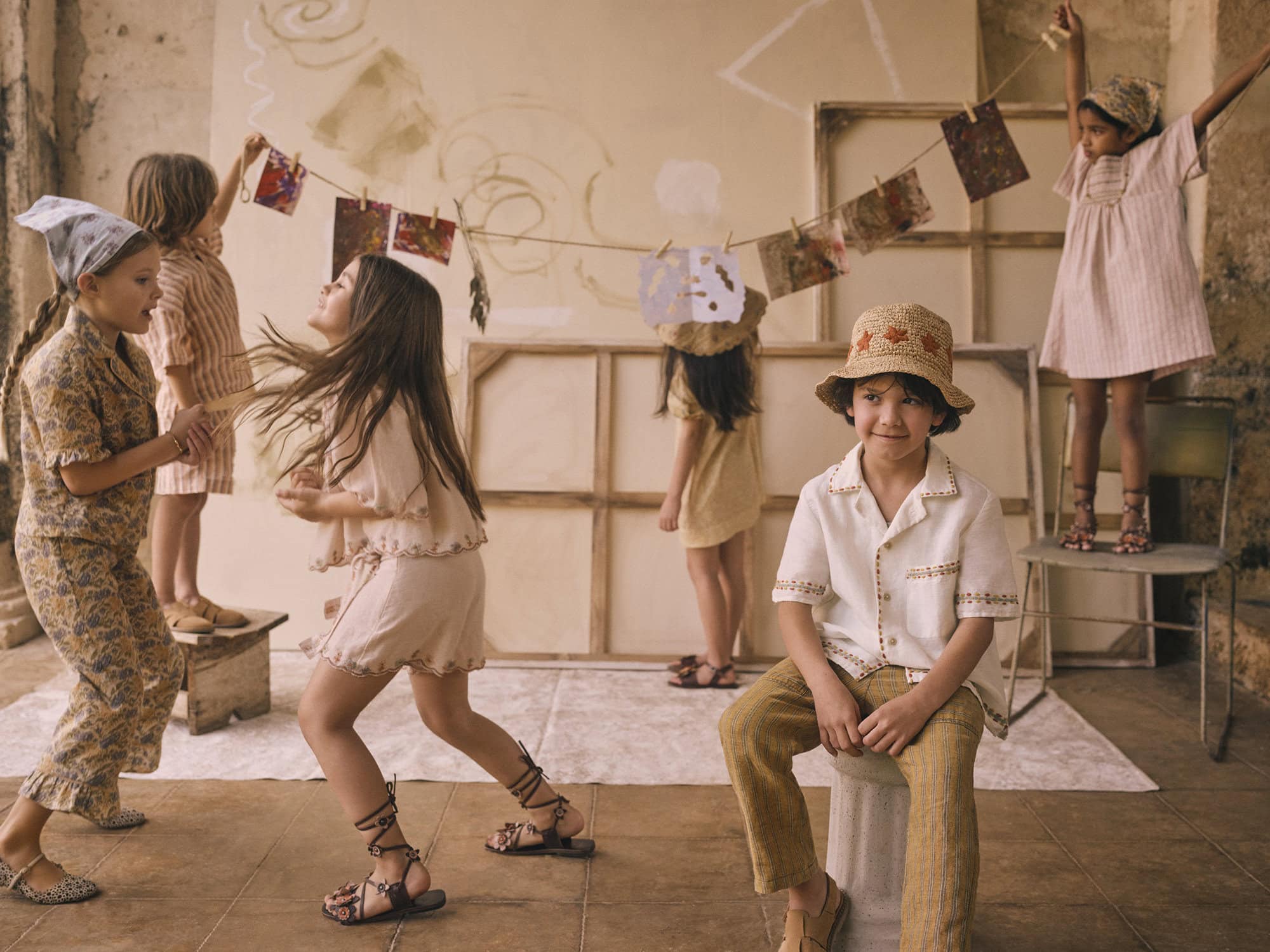 Group of children in retro-style clothing in a casual indoor setting with hanging artwork, creating a playful, vintage-inspired aesthetic.