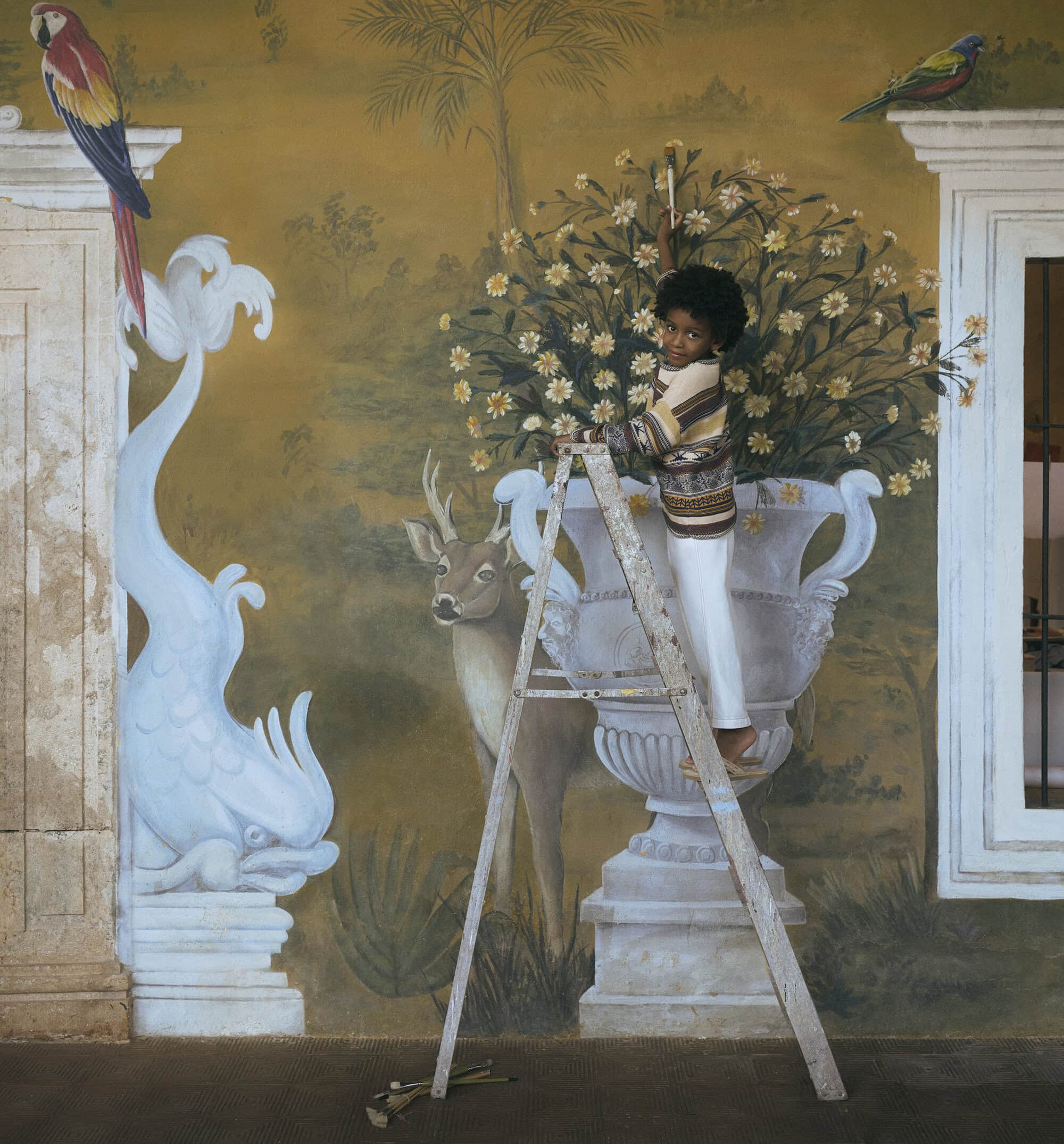 A painterly image shows a child standing on a ladder painting a mural-style wall with painted birds, flowers, and a deer in earthy tones.