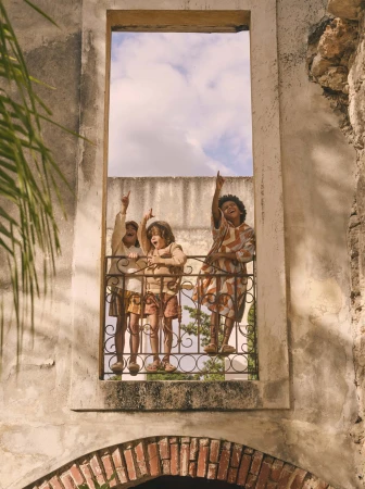 Three kids of varying ethnicities stand behind a wrought iron railing, looking up and pointing, framed by a weathered stone archway.
