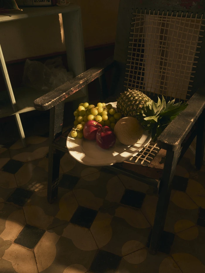 A white plate holding grapes, apples, a melon, and a pineapple resting on an antique wooden chair.