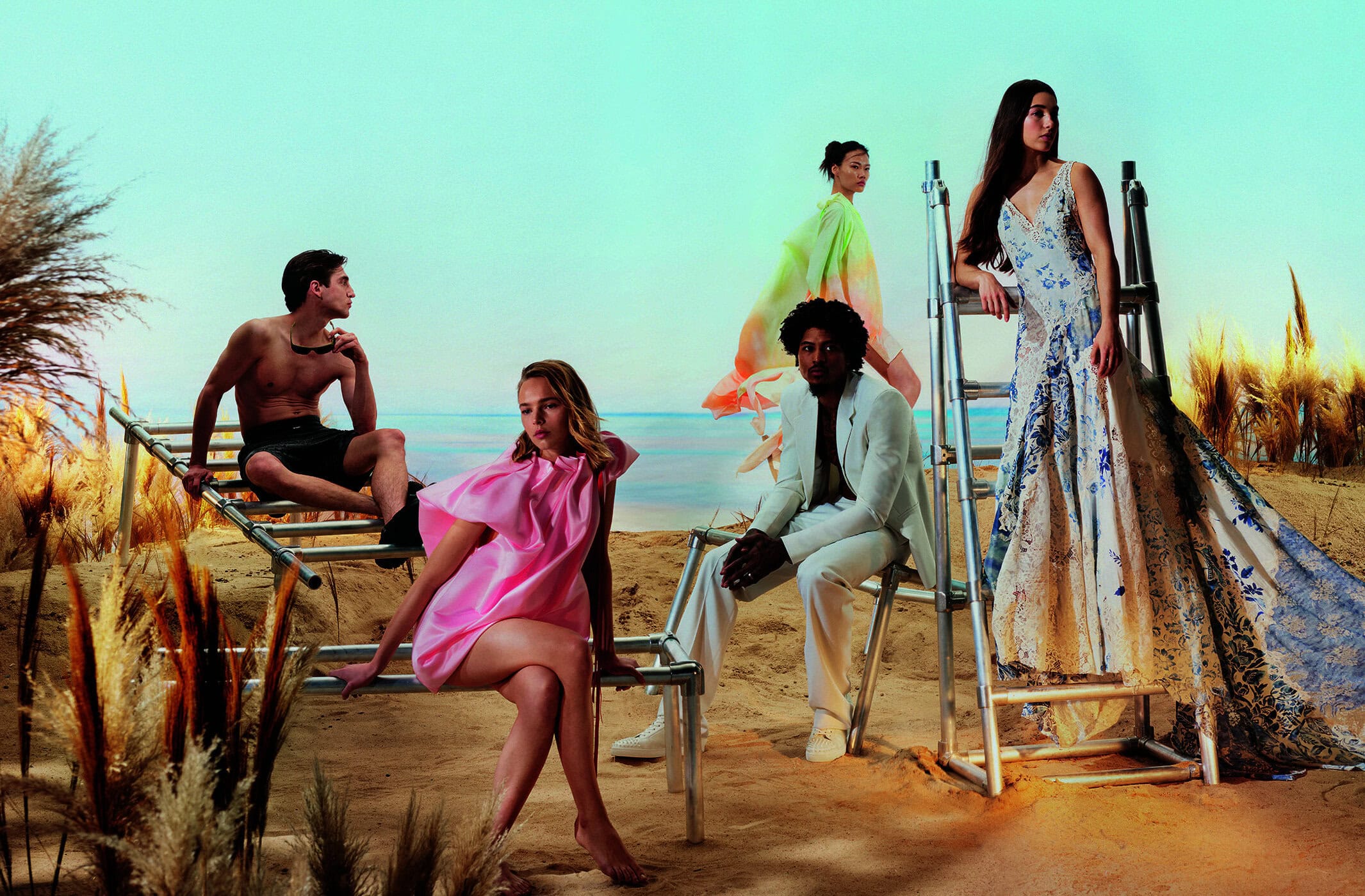 Fashion editorial shot of five people posing on a beach, wearing a mix of swimwear, dresses, and suits in a light and airy aesthetic.