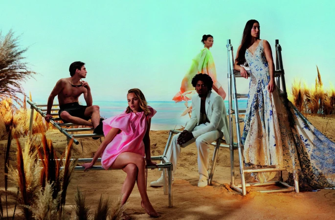 Fashion editorial shot of five people posing on a beach, wearing a mix of swimwear, dresses, and suits in a light and airy aesthetic.