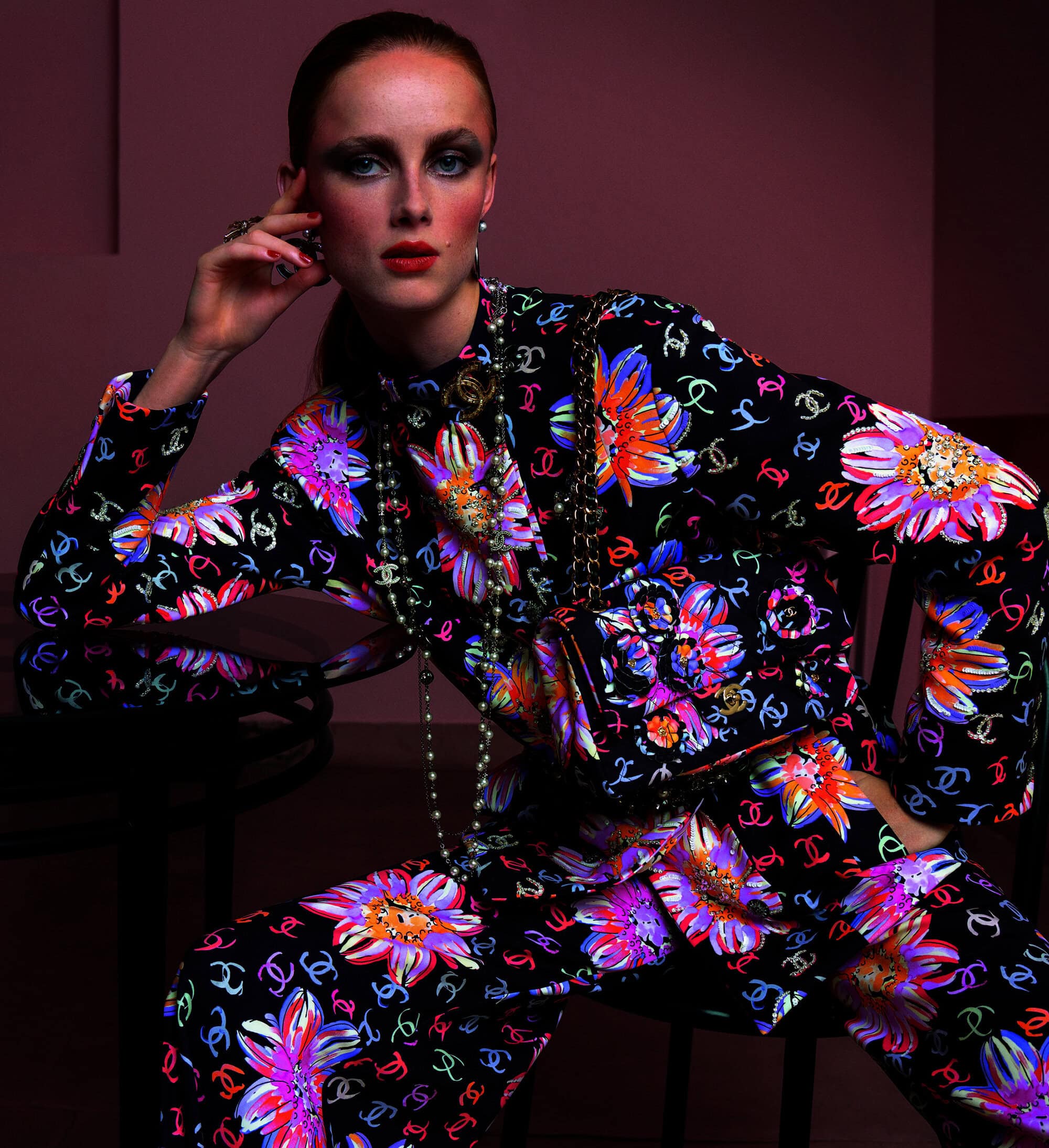 Fashionable woman in floral print suit and gold accessories poses in studio with red lips, smokey eye makeup and slicked back hair.