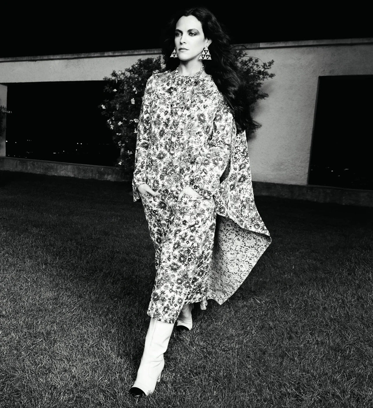 Model in patterned coat and white boots walking on lawn outdoors at night for Chanel Spring 2024 campaign